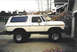 1979 Ford Bronco - Lifted 1979 Ford Bronco in a driveway, showing its side profile and large off-road tires.