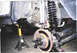 1979 Ford Bronco - The vehicle's front suspension is supported by a jack stand, revealing the coil spring and shock absorber.