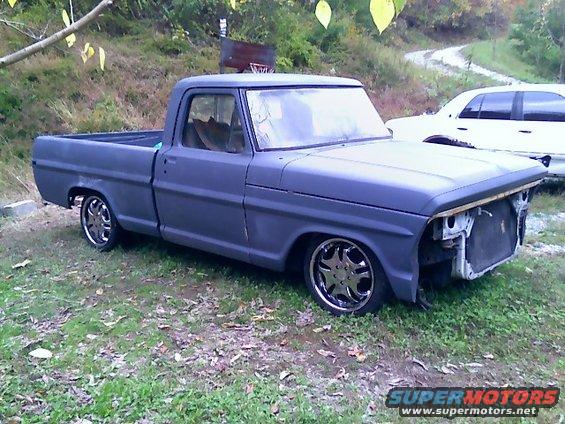 Gray Ford pickup truck with custom wheels, missing grille, parked on grass
