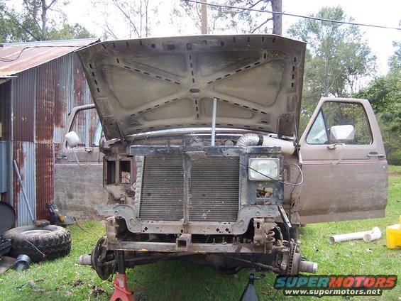 Front end of a disassembled truck with hood open, doors open, and grille removed