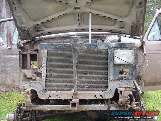 Truck front end with hood open, showing radiator and engine components. Some parts are missing