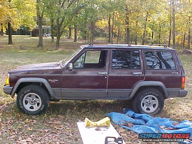 Maroon Jeep Cherokee parked on grass with trees in background