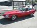 1962 Jaguar XKE - A red 1962 Jaguar XKE coupe is parked curbside near a bus stop.
