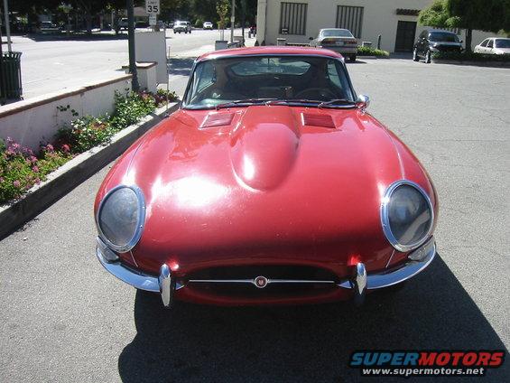 Front view of a red classic sports car with a prominent hood scoop and chrome bumper