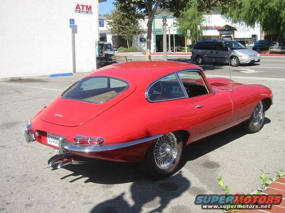Red 1962 Jaguar XKE coupe parked on asphalt, rear quarter view. Wire wheels and chrome bumpers visible