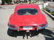 1962 Jaguar XKE - The rear of a red Jaguar E-Type coupe is shown, chrome bumpers and dual exhaust pipes.