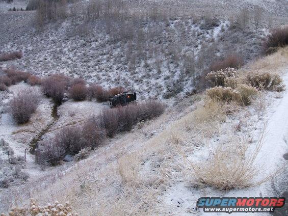 Black truck overturned on a snowy hillside next to brush