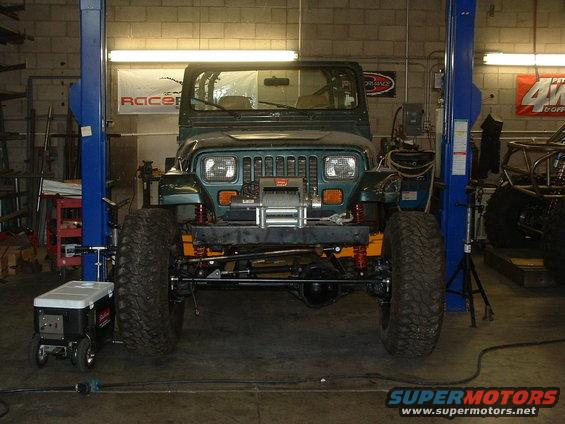 Green Jeep Wrangler on a lift in a garage, has a winch on the front bumper