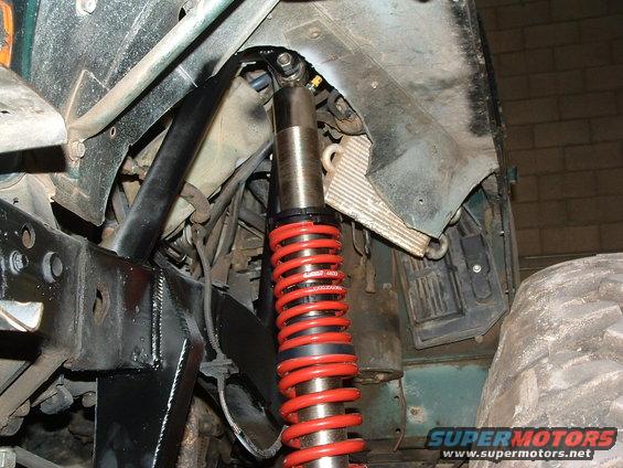Close-up of a red coilover shock absorber mounted to the frame of an off-road vehicle