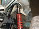 1994 Jeep YJ - The suspension system of an off-road vehicle, a red coilover shock absorber and exposed frame components.