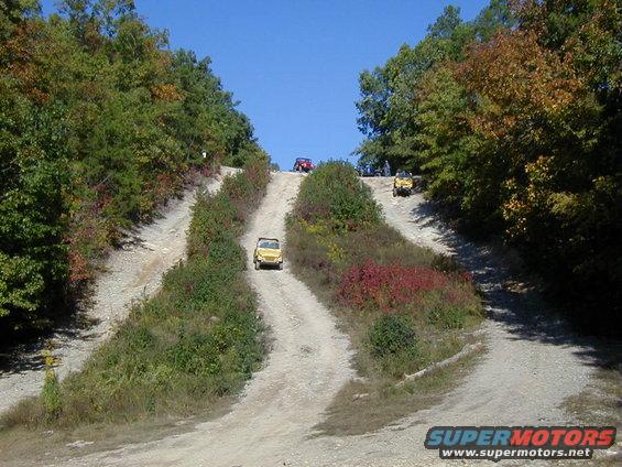 Yellow off-road vehicle climbing a dirt hill, with other vehicles behind it