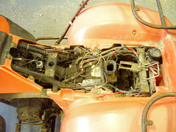 Orange ATV engine compartment with exposed wiring and components. The body panels are removed, revealing the engine and associated parts