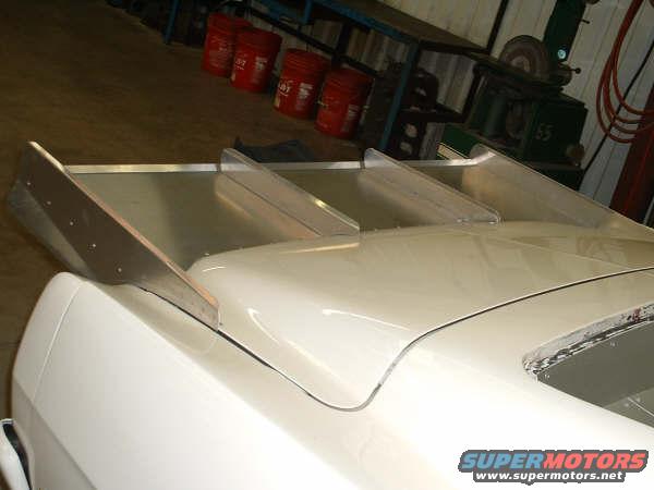 White car's rear with a large, multi-level aluminum spoiler. Visible Supermotors.net logo