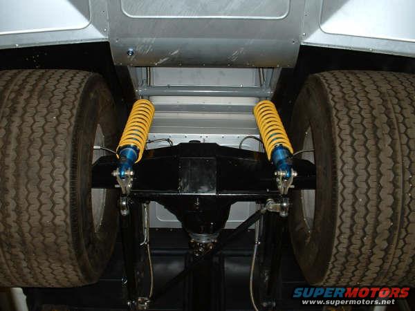 Underside view of a vehicle's rear axle with yellow coilover shocks and large tires