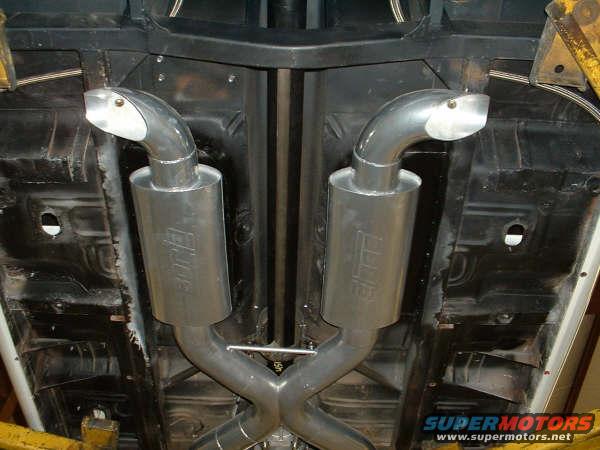 Underside of a vehicle showing a dual exhaust system with polished mufflers and angled tips