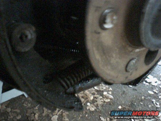 close-up of a car's brake drum and shoe assembly, showing a spring and some dirt
