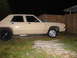 1985 Ford Crown Victoria LTD - Side view of a tan sedan with custom wheels and exhaust pipes, parked in a yard at night.