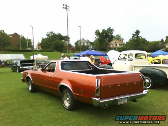 Orange Ford Ranchero pickup truck parked on grass at car show, other vehicles and tents in background
