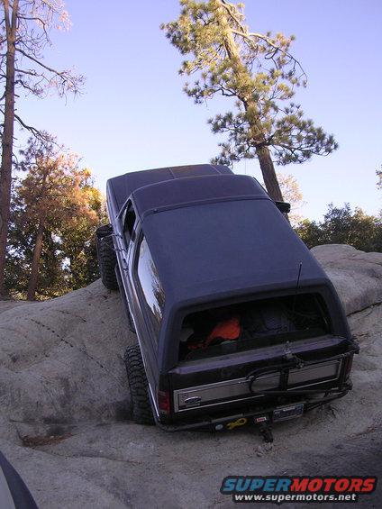 Dark SUV with aftermarket bumper and spare tire carrier on a rocky trail