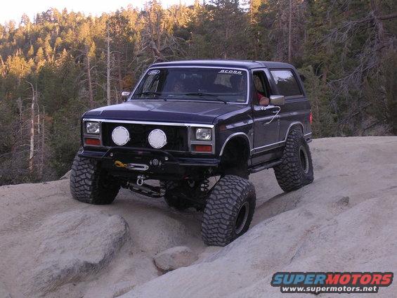 Dark blue 1984 Ford Bronco II with large off-road tires navigating rocky terrain