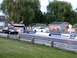 2003 Ford Crown Victoria - Two sedans are lined up on a drag strip, ready for a race, with a small building and trees visible.