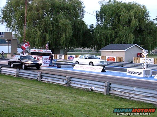 Two 2003 Ford Crown Victorias at a drag strip, one black, one white, viewed from the front