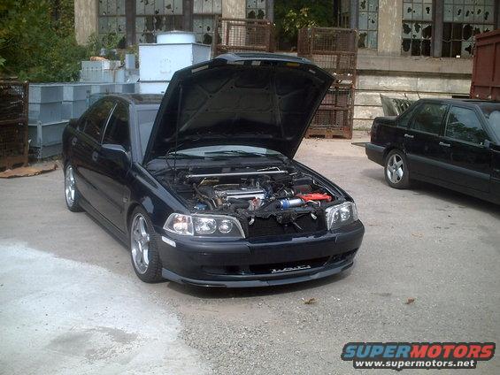 Dark sedan with hood open, showing engine bay. Another black sedan parked behind it