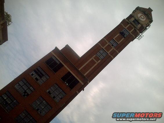 Clock tower with a 'P' logo against a cloudy sky