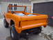 1977 Ford Bronco - This orange Ford Bronco is missing its doors and top, parked in front of a garage.