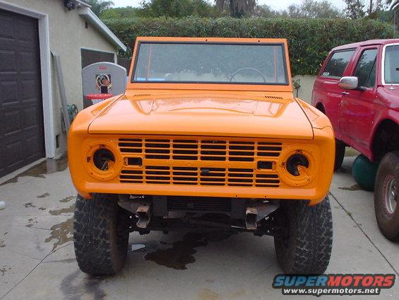 1977 Ford Bronco front end, orange paint, missing headlights, parked next to a red SUV