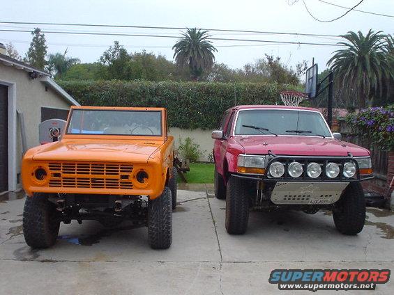 Orange first-gen Bronco next to a red later-model Bronco with a brush guard and lights