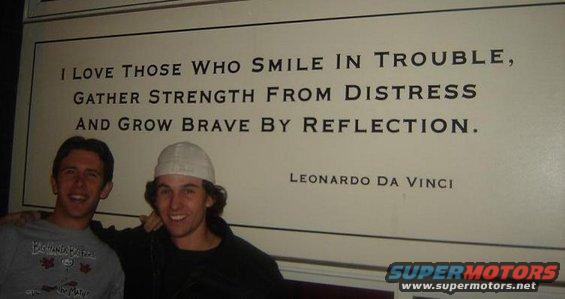 Two guys smiling in front of a wall with a quote by Leonardo Da Vinci