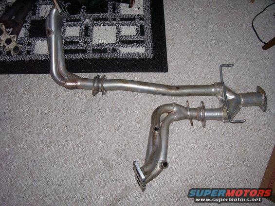 Exhaust manifold and pipe assembly on carpet. Includes a Supermotors.net watermark