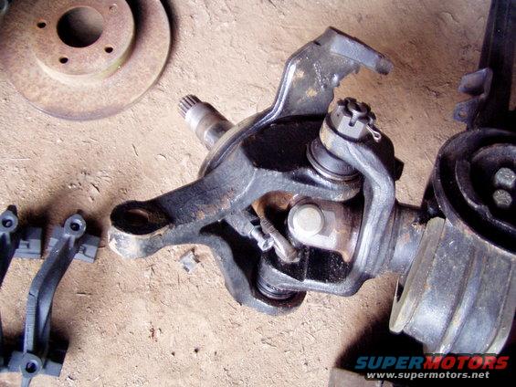 Front axle assembly with brake rotor and suspension components on a dirt surface