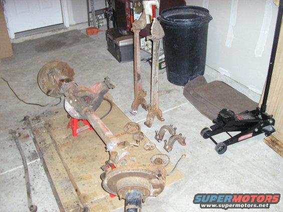 Rusty rear axle assembly on red jack stands with a floor jack and other parts