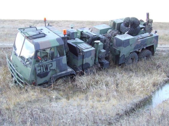 Camouflaged military truck with '31W2' on the side, stuck in a ditch