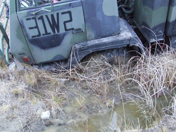 Green military truck with black markings stuck in muddy terrain