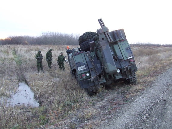Military truck tilted in a ditch with soldiers standing nearby