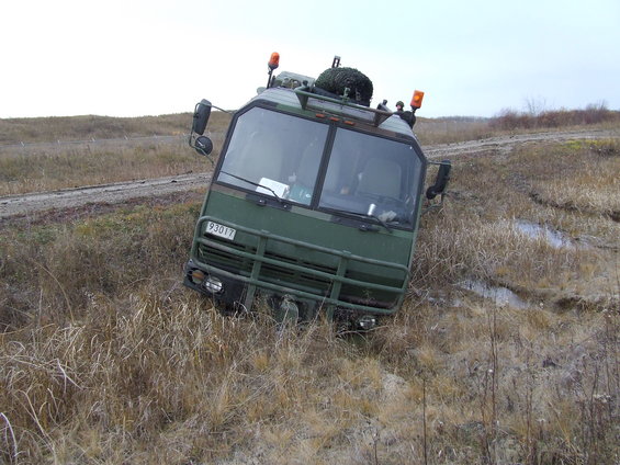 Green military truck tilted in grassy ditch with orange lights on top
