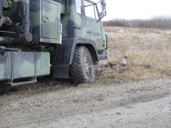 Camouflaged military truck with large tire stuck in mud