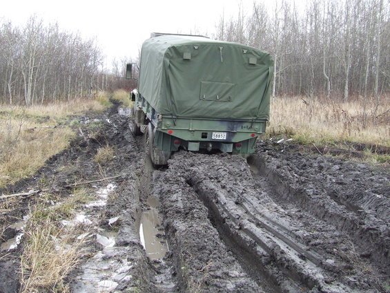 Green military truck stuck in deep mud on a dirt track, rear view