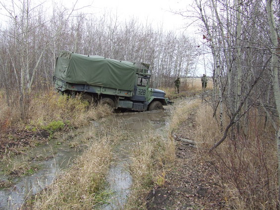 Military truck stuck in a muddy ditch with two soldiers standing nearby