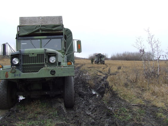 Green military truck stuck in mud, another truck in background