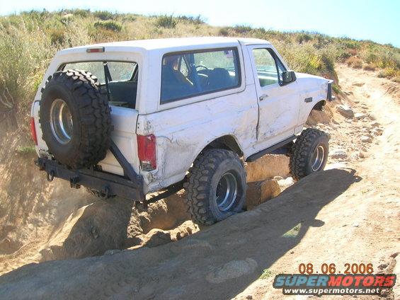 White Ford Bronco with a spare tire on the back, navigating a rocky off-road trail
