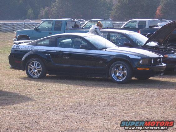 Black Ford Mustang GT with silver racing stripes, parked next to other vehicles