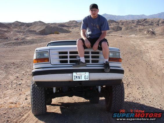 Guy sitting on the front of a lifted white Ford F-150. California plate reads IMNT OJ