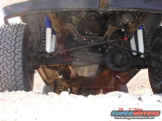 Undercarriage of a 1996 Ford Bronco with off-road tires and blue/white shocks