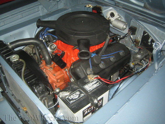 car engine bay with orange block, black air cleaner, and battery