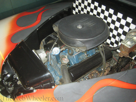 Engine bay with blue engine block, black air cleaner, and flame graphics on the fender. Checkered flag pattern visible in background