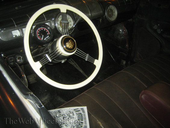 Car interior with a white steering wheel, brown leather seats, and a newspaper on the floor